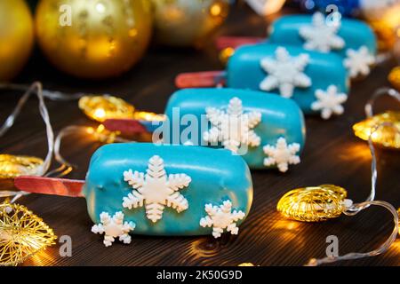 Blaues weihnachtliches Dessert in Form von Mousse auf einem mit Schneeflocken geschmückten Stock auf einem Hintergrund glühender Girlanden Stockfoto