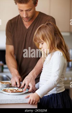 Gute Essgewohnheiten vermitteln. Ein kleines Mädchen, das mit ihrem Vater Frühstück macht. Stockfoto