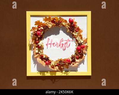 Rahmen mit Blumenkranz. Boho-Kranz aus trockenen Herbstblättern und Beeren. Wort Herbst bedeutet Herbst in deutscher Sprache. Saisonaler Herbst flach lag auf Stockfoto