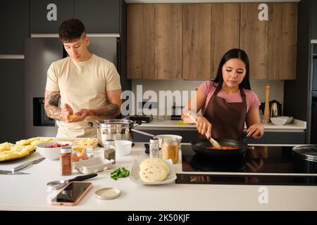Zwei junge lateinamerikaner Formen Llapingachos-Teig und kochen in einer Pfanne. Stockfoto