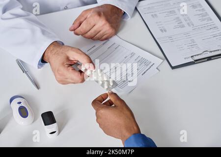 Nahaufnahme eines Arztes, der dem Patienten Medikamente gibt, während er am Tisch sitzt Stockfoto