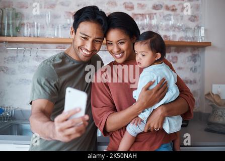 Glücklich, Eltern und Baby mit Down-Syndrom nehmen Selfie zusammen in der Küche des Familienhauses. Glück, Lächeln und Mutter und Vater verbinden sich mit Stockfoto