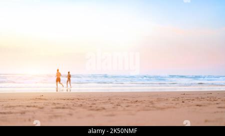 Ein Paar läuft am Strand. Ein glückliches Paar geht zum Sonnenuntergang ins Meer. Verschwommener Hintergrund für Sommerferien. Unverschämter Mann und Frau laufen am Sandstrand. Sommerzeit. Glückliche Menschen Stockfoto