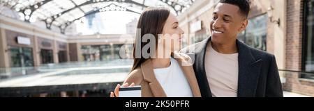 Glückliche junge Frau mit Kreditkarte in der Nähe trendigen afroamerikanischen Freund, Banner, Stock Bild Stockfoto