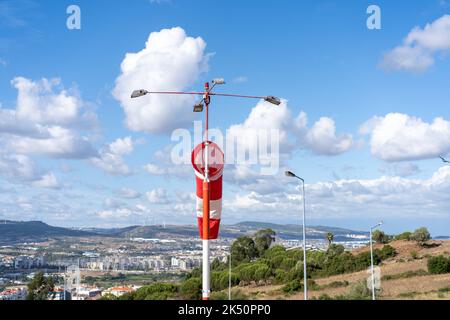 Windsocken fliegen. Sommer heißen Tag auf privaten sportlichen Flughafen mit verlassenen Windsack, Wind weht und Windsack ist faul in Bewegung. Windsack mit Wolkenhimmel Berg und Straße mit Autos im Hintergrund Stockfoto