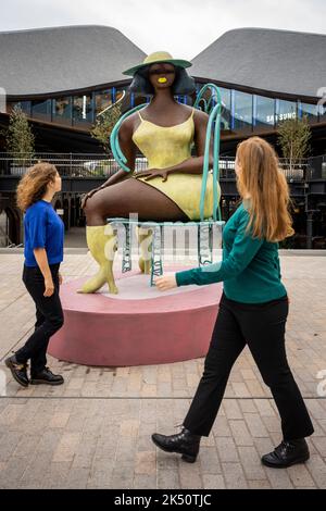 London, Großbritannien. 5. Oktober 2022. Frauen gehen am Coal Drops Yard in der Nähe von King’s Cross vorbei an Tschabalala Self's ‘Seated’, einem neu enthüllten öffentlichen Werk im Auftrag von Avant Arte. Die großformatige Bronze steht mit fast 3 Metern Höhe und ist die erste öffentliche Skulptur des Künstlers. Kredit: Stephen Chung / Alamy Live Nachrichten Stockfoto