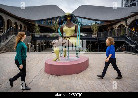 London, Großbritannien. 5. Oktober 2022. Frauen gehen am Coal Drops Yard in der Nähe von King’s Cross vorbei an Tschabalala Self's ‘Seated’, einem neu enthüllten öffentlichen Werk im Auftrag von Avant Arte. Die großformatige Bronze steht mit fast 3 Metern Höhe und ist die erste öffentliche Skulptur des Künstlers. Kredit: Stephen Chung / Alamy Live Nachrichten Stockfoto