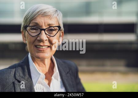 Porträt einer erfolgreichen Geschäftsfrau im Freien. Ein glücklicher Geschäftsmann lächelt und schaut in die Kamera. Stockfoto