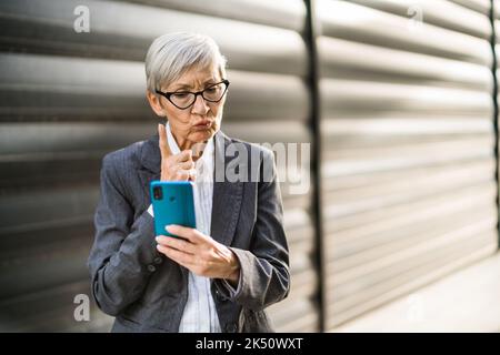 Außenportrait einer Geschäftsfrau, die auf dem Smartphone chattet. Sie ist wütend. Stockfoto