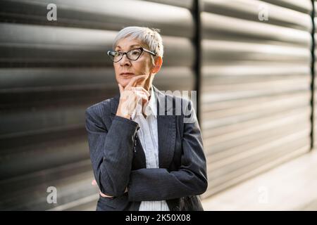 Außenportrait einer nachdenklichen Geschäftsfrau vor dem Firmengebäude. Stockfoto