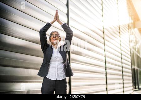 Außenportrait einer Geschäftsfrau, die vor dem Firmengebäude meditiert. Stockfoto