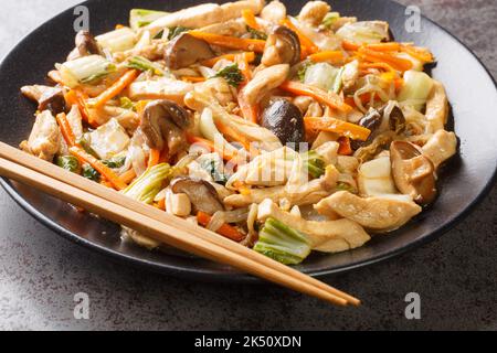 Hacken Sie die mit Hühnchen gemachten Saeues schnell mit knackigem gemischtem Gemüse und Bohnensprossen in einer dicken braunen Soße in Nahaufnahme auf einem Teller auf dem Tisch. Hori Stockfoto