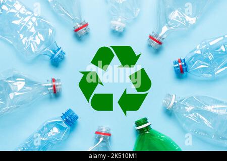 Leere zerknitterte Plastikflaschen auf blauem Hintergrund mit Recycling-Symbol in der Mitte Stockfoto