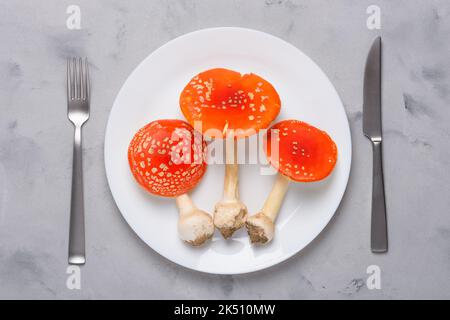 Amanita muscaria fliegen agarische giftige Pilze auf Teller mit Gabel und Messer Draufsicht. Verbrauch von halluzinogenen Pilzen Konzept Stockfoto