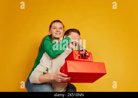 Porträt von liebenden Paar, Mann und Frau feiern Ferien, Überraschung mit Geschenken isoliert auf gelbem Hintergrund Stockfoto