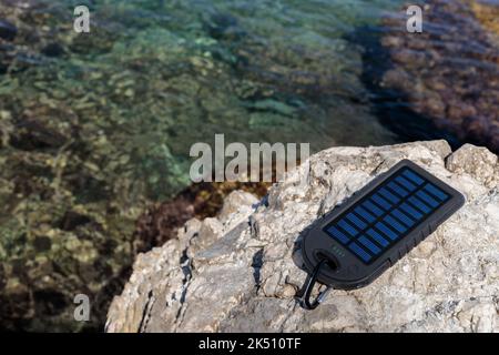 Batterie-Solaranlage vor dem Hintergrund eines schönen Strandes. Laden Sie Ihr Smartphone über den Solarakku. Stockfoto