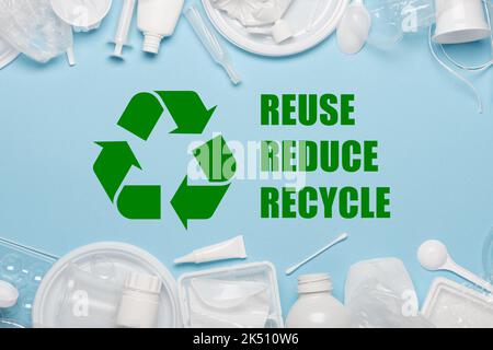 Recycling-Sybmol mit Reuse Reduce Recycle Slogan umgeben von Einweg-Kunststoffobjekten, Verpackung von Kunststoffprodukten auf blauem Hintergrund Stockfoto