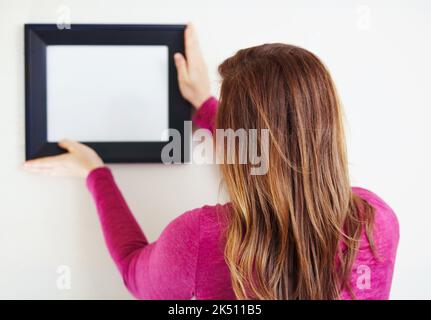 Hängen Sie Ihren Copyspace auf. Rückansicht einer jungen Frau, die einen Bilderrahmen aufstellt. Stockfoto