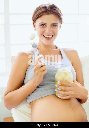 Sich ihrem Verlangen hingeben. Eine Schwangerin, die eingelegte Zwiebeln aus einem Glas isst - Porträt. Stockfoto