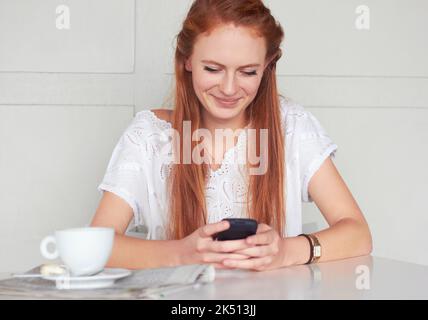 Ich bekam einen Tisch. Eine schöne junge Frau benutzte ihr Handy in einem Café. Stockfoto