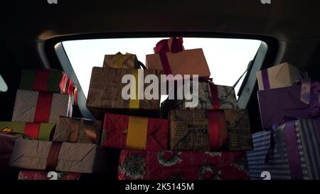 weihnachtsmann liefert Geschenke. Geschenke vom weihnachtsmann. Lieferservice. Deliveryman entlädt Boxen. Geschenk-Boxen im Auto. Schön verpackte Pakete. Blick aus dem Inneren des Autos. Spende, Wohltätigkeit oder Lieferkonzept. Hochwertige Fotos Stockfoto