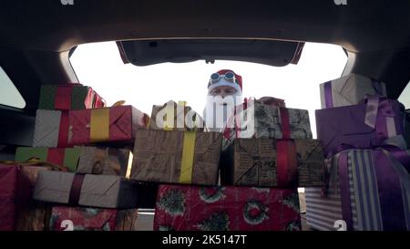 weihnachtsmann liefert Geschenke. Geschenke vom weihnachtsmann. Lieferservice. Deliveryman lädt Boxen. Geschenk-Boxen im Auto. Schön verpackte Pakete. Blick aus dem Inneren des Autos. Spende, Wohltätigkeit oder Lieferkonzept. Hochwertige Fotos Stockfoto