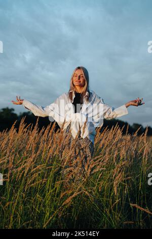 Junge blonde Frau, die weit weg schaut, inmitten des Weizenfeldes stehend, grüblend. Stockfoto