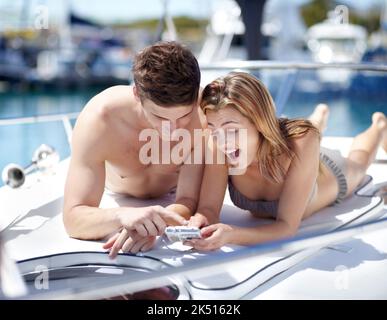 Ich liebe dieses Foto. Junges Paar, das sich ihre Urlaubsfotos anschaut, während es sich auf einer Yacht entspannt. Stockfoto