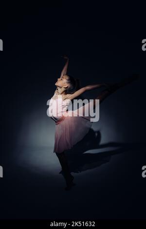 Ballerina Kind Mädchen in rosa Kleid Tänze durch Licht auf dunklem Hintergrund beleuchtet. Stockfoto