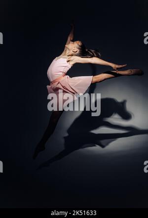 Ballerina Kind Mädchen in rosa Kleid Tänze durch Licht auf dunklem Hintergrund beleuchtet. Stockfoto