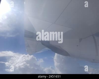 Ein schöner Blick auf den Himmel und ein Motor eines ATR-Fluges vom Passagierfenster tagsüber an einem heißen, sonnigen Tag mit Wolken am blauen Himmel. Stockfoto