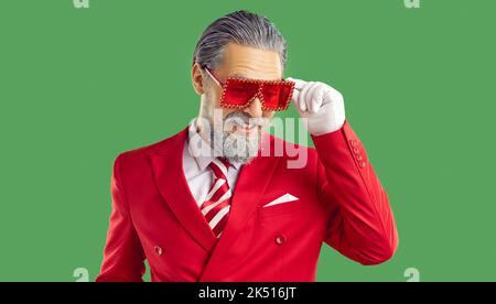 Der alte Mann im roten Anzug und einer Brille im Weihnachtsmann-Stil blickt auf grünen Hintergrund. Stockfoto