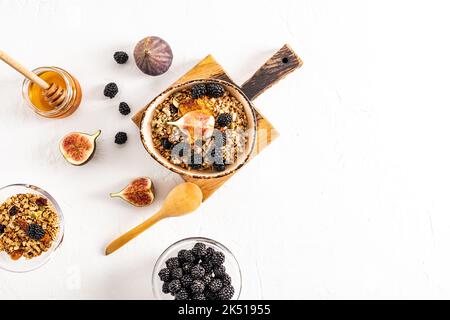 Leckeres gesundes Müsli mit getrockneten Früchten und Honig, frischen Brombeeren und Feigen in einer Keramikschale auf einem Schneidebrett. Draufsicht. Weißer Hintergrund Stockfoto