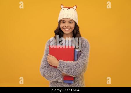 Glückliches Kind in Pullover und Hut halten Arbeitsbuch auf gelbem Hintergrund, Bildung Stockfoto