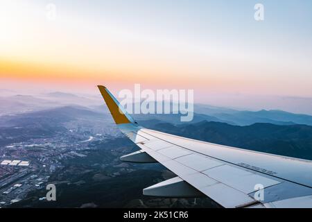 Atemberaubende Aussicht auf die Stadt und wolkenloser Sonnenuntergang hinter dem Flugzeug während des Fluges Stockfoto