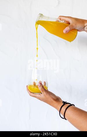 Crop unkenntlich Person Gießen frischen gesunden Orangensaft aus der Flasche in das Glas vor weißem Hintergrund Stockfoto