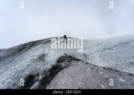 Von unten klettern unerkennbare Bergsteiger auf gefrorenen Klippen des Vatnajokull Glacier gegen bewölkten grauen Himmel am kalten Wintertag in Island Stockfoto