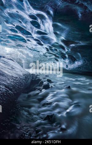 Am Frühlingstag in Island fallen aus der blauen Decke der Eishöhle auf felsigen Grund im Vatnajokull-Gletscher Wassertröpfchen Stockfoto