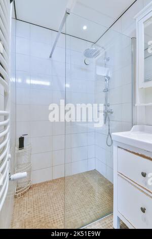 Duschhähne, die an der gefliesten Wand in der Nähe der Glaswand und der Zierschwanzwand im Waschraum zu Hause angebracht sind Stockfoto