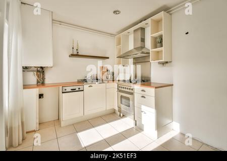Interieur der hellen Küche mit weißen Schränken und eingebautem Herd und Waschbecken auf der Theke Stockfoto