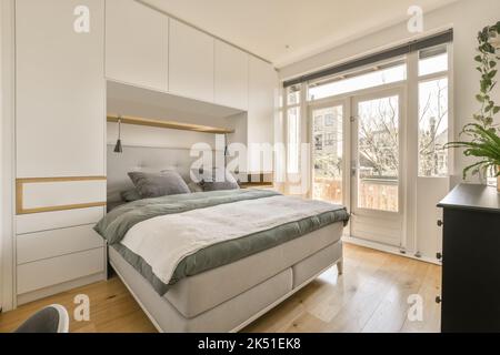 Moderne Einrichtung im Schlafzimmer mit bequemem weichen Bett und Lampen in der Nähe des eingebauten Kleiderschranks bei Tageslicht Stockfoto