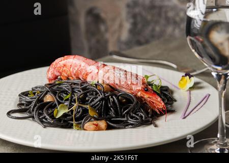 Schwarze Spaghetti mit Tintenfisch, garniert mit Garnelen und Sprossen, serviert auf dem Teller während des Mittagessens im Restaurant Stockfoto