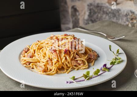 Leckere Spaghetti mit Carbonara-Gericht mit Speck und Parmesan, gemischt mit Ei, serviert auf dem Teller mit Sprossen und Blumen während des Mittagessens im italienischen Restaurant Stockfoto
