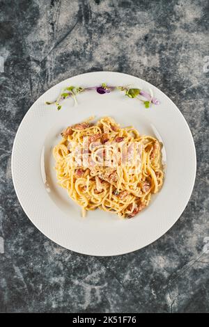 Leckere Spaghetti mit Kohlensäure, Speck und Parmesan, gemischt mit Ei, serviert auf dem Teller mit Sprossen und Blumen während des Mittagessens in italienischer Sprache Stockfoto