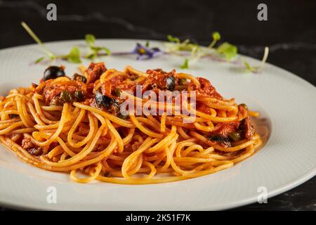 Closeup leckere Spaghetti alla puttanesca Gericht mit Tomatensauce und Meeresfrüchten garniert mit Knoblauch und Chili-Pfeffer und serviert auf dem Teller in italienischen Resta Stockfoto