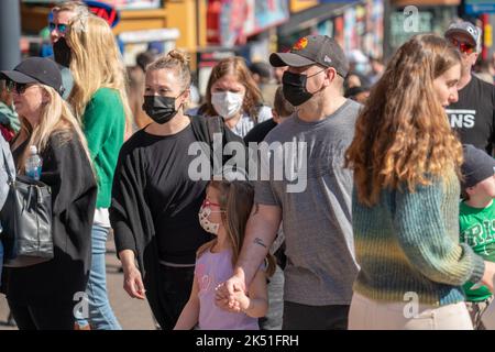 Menschenmassen, die die Clifton Hill Street mit schwarzen Covid-19-Masken in Niagara, Ontario, Kanada, entlang laufen. Tourismusgebiet in der Pandemie von 2022. Stockfoto