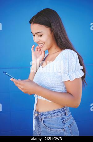 Telefon, soziale Medien und Kommunikation mit einer Frau auf blauem Hintergrund für Networking oder Konnektivität. App, Smile und 5G Mobiltechnologie mit einem Stockfoto