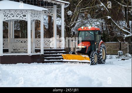 Jurmala, Lettland, 25. Dezember 2021: Ein Schneeräumtraktor reinigt das Gelände im Park. Kommunaler Service Reinigung Bürgersteig von Schnee. Stockfoto