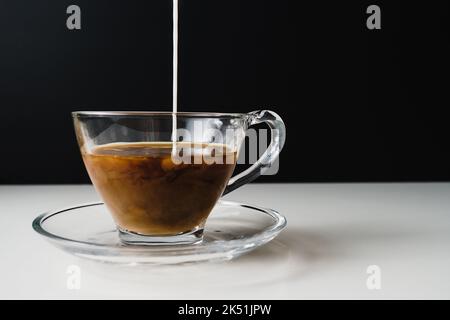 Milch wird in die Kaffeetasse gegossen. Vor schwarzem Hintergrund mit verfügbarem Kopierplatz Stockfoto