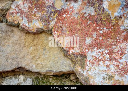 Textur der alten verputzten Wand mit Überresten von Farbe, Risse und grünem Moos. Hintergrund einer schäbigen Gebäudeoberfläche. Zerstörte Wand mit abgefallener Gips Stockfoto